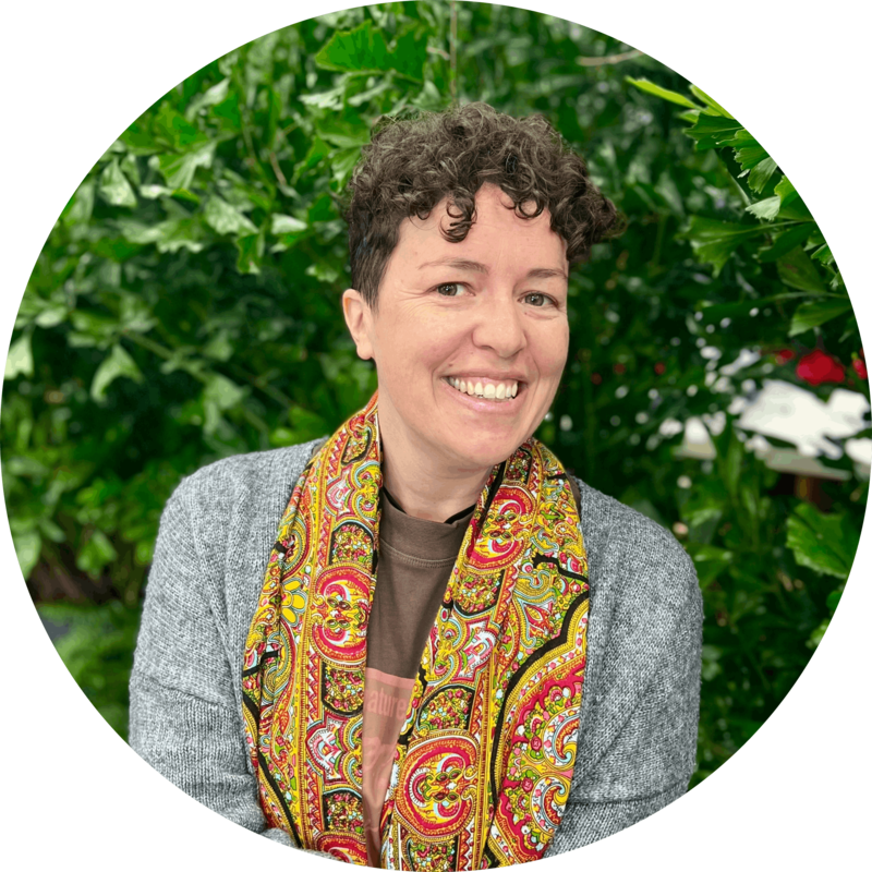A close-up circular portrait of Coach Pau smiling outdoors, with short curly hair, a grey cardigan, and a colorful Galician scarf.