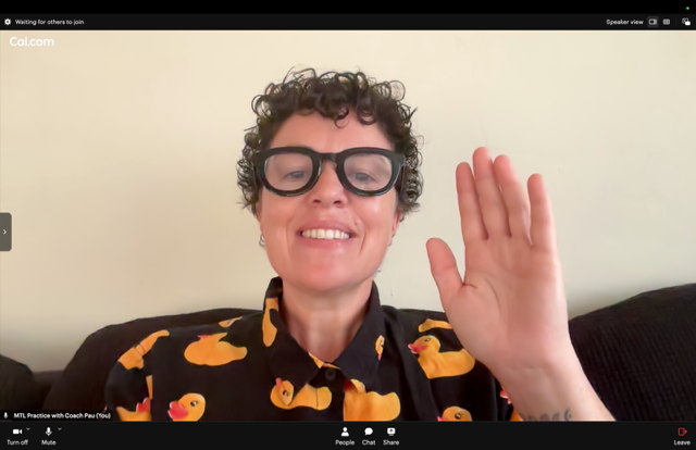 Coach Pau smiling and waving on a video call, with short curly hair, thick black-rimmed glasses, and a black rubber-duck patterned shirt.